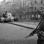 A Hungarian solder, whose armband indicates that he has joined the freedom-fighters, stands in front of a disabled Soviet tank. Budapest, Hungary. October-November, 1956.