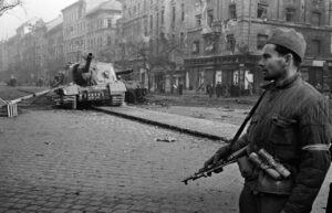 A Hungarian solder, whose armband indicates that he has joined the freedom-fighters, stands in front of a disabled Soviet tank. Budapest, Hungary. October-November, 1956.